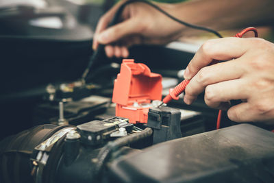 Cropped hands charging battery of car with electric cables