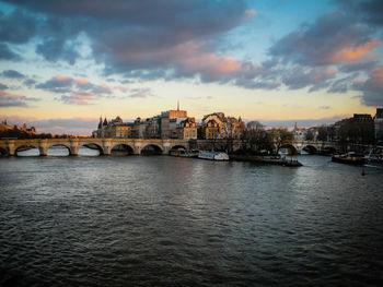 Bridge over river in city against sky at sunset