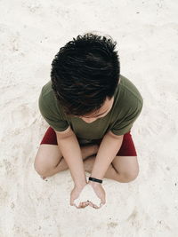 High angle view of man holding sand in heart shape while sitting at beach