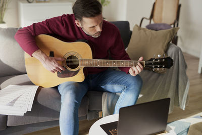 Midsection of man playing guitar at home