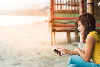 Side view of young woman using mobile phone at beach