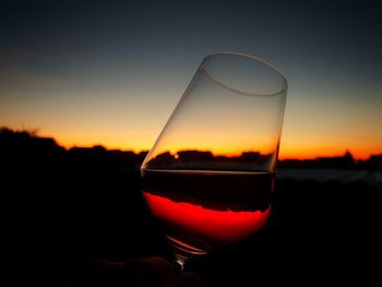 Close-up of hand holding beer glass against sunset