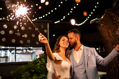 Happy bridegroom holding sparklers at night