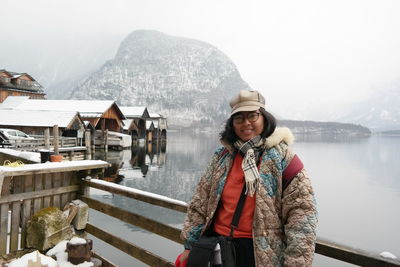 Portrait of smiling woman wearing warm clothing while standing against river during winter