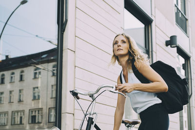 Female executive with bicycle standing against building in city