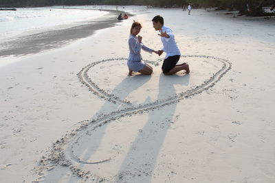Portrait of couple kneeling amidst heart shape on sand at beach