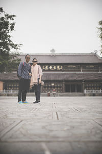Full length portrait of couple standing against building 