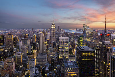 Illuminated buildings in city against cloudy sky