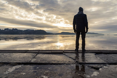 Rear view of man standing on shore at beach against sky