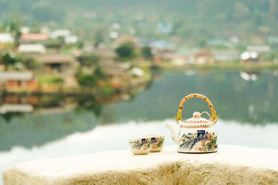 Close-up of chinese teapot and teacups outdoors with lake and village scenery