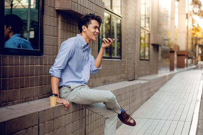 Smiling man talking on phone while sitting in by building in city