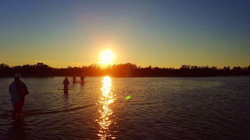 Silhouette people by sea against clear sky during sunset