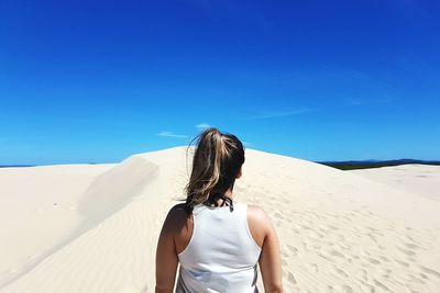 Rear view of woman standing on sand dune against blue sky