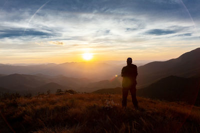 Rear view of man standing on mountain against sky during sunset