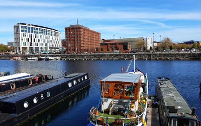 Boats in river by buildings in city against sky