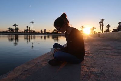 Side view of man sitting on swimming pool at sunset