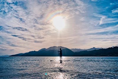 Silhouette person paddleboarding on sea against sky