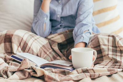 Midsection of woman using mobile phone on bed at home