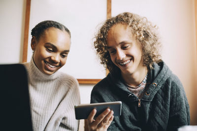 Male and female teenagers smiling while looking at smart phone in room