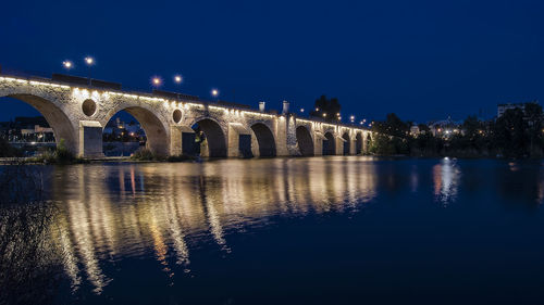 Illuminated bridge over water in city at night