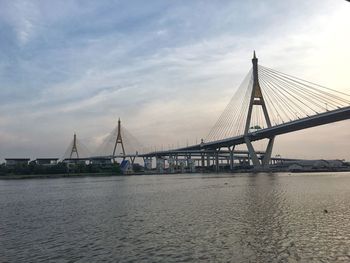 View of suspension bridge over river against cloudy sky
