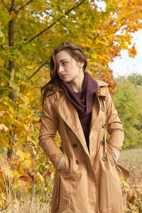 Woman wearing coat standing against trees in park during autumn