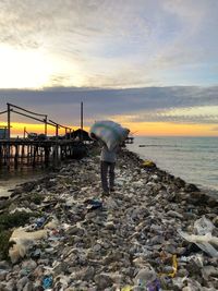 Man on garbage at shore against sky during sunset