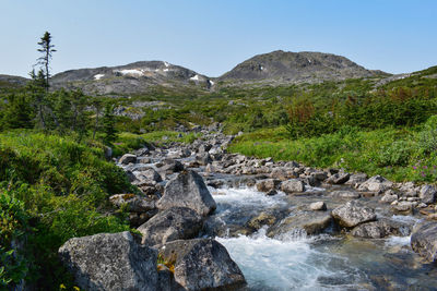 Stream flowing through rocks against sky