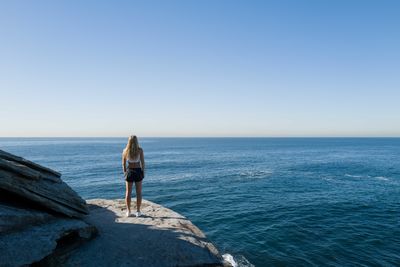 View from behind of a woman standing on the cliff overlooking the ocean