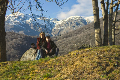 Mother and children rest on a granite rock in the shade of trees along an alpine path in italy