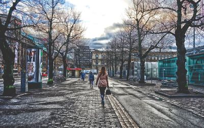 Rear view of woman walking on snow covered bare trees in city