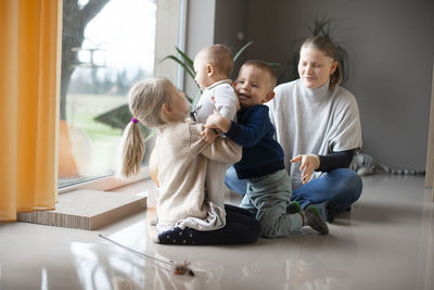 Mother with her three children playing with a cat on the floor at home