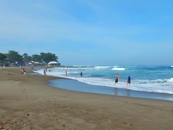 People standing on beach against clear blue sky