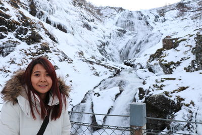 Portrait of smiling woman standing against snowcapped mountain 