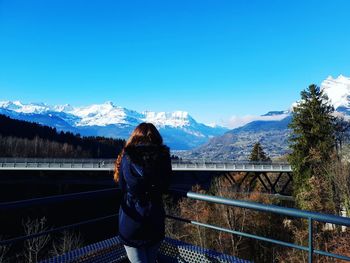 Rear view of woman looking at mountains against clear blue sky