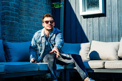 Portrait of young man throwing bottle while sitting on sofa