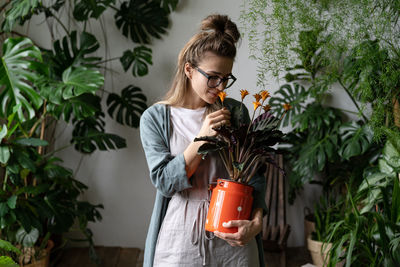 Young woman holding plant while standing against potted plants