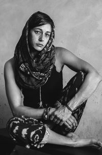 Portrait of young woman sitting on bench against wall at home