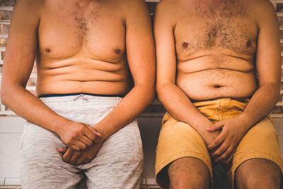 Midsection of shirtless men sitting against wall