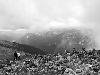 Rear view of friends standing on mountain against cloudy sky during winter