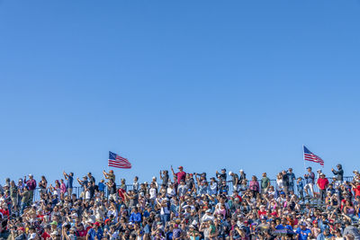 Group of people at flags against clear blue sky