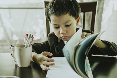 Boy reading book while sitting on table