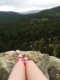 Low section of woman legs on cliff against sky