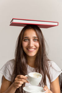 Portrait of woman holding coffee cup with book on head