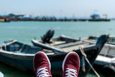 Low section of person wearing shoes against boats in lake