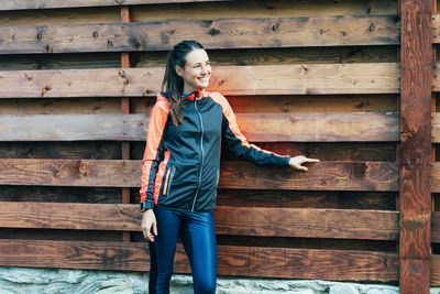 Portrait of young woman standing against wooden wall