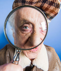 Portrait of senior woman looking through magnifying glass against blue background