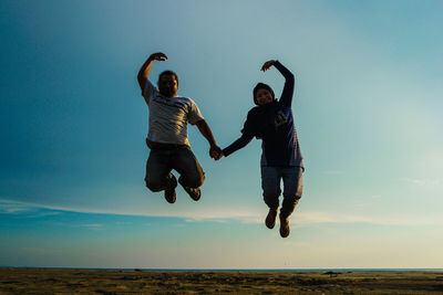 Full length of friends with arms raised jumping against sky