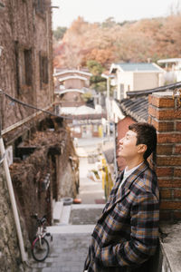 Side view of boy standing against buildings in city