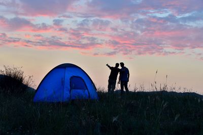 Silhouette friends camping on field against sky